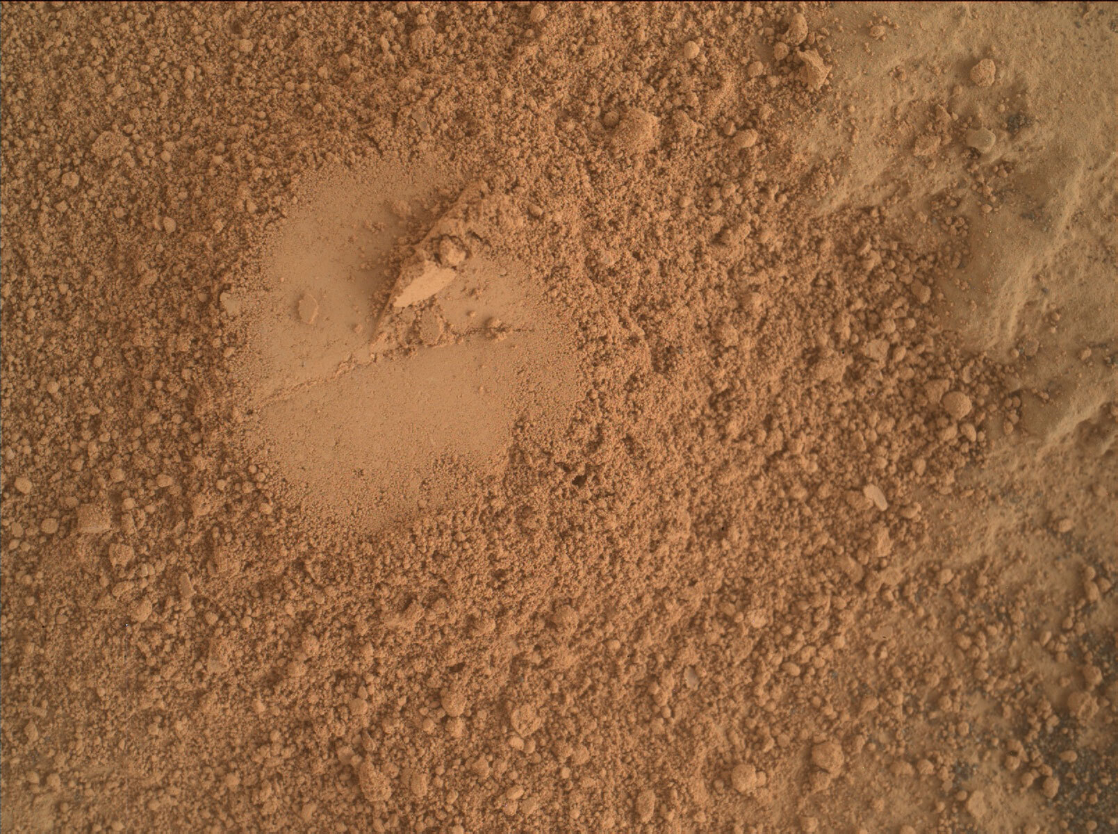 This is a colored image of sand and rock scattered on a smooth surface. On the center of the image, a smooth circular surface is present.