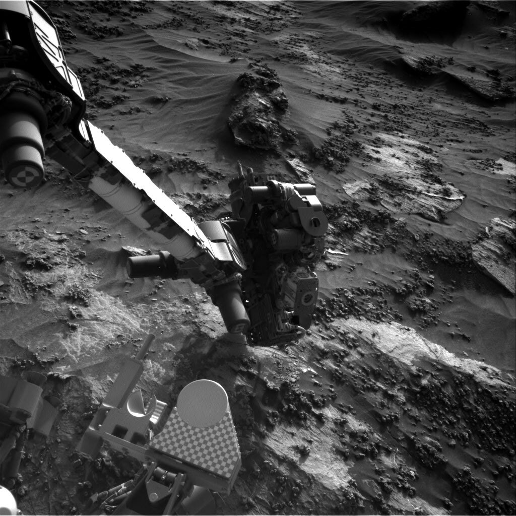 This is a black and white image of the sandy, rocky terrain on Mars. Very small smooth hills and some very rough textured rocks can be seen in the image. 