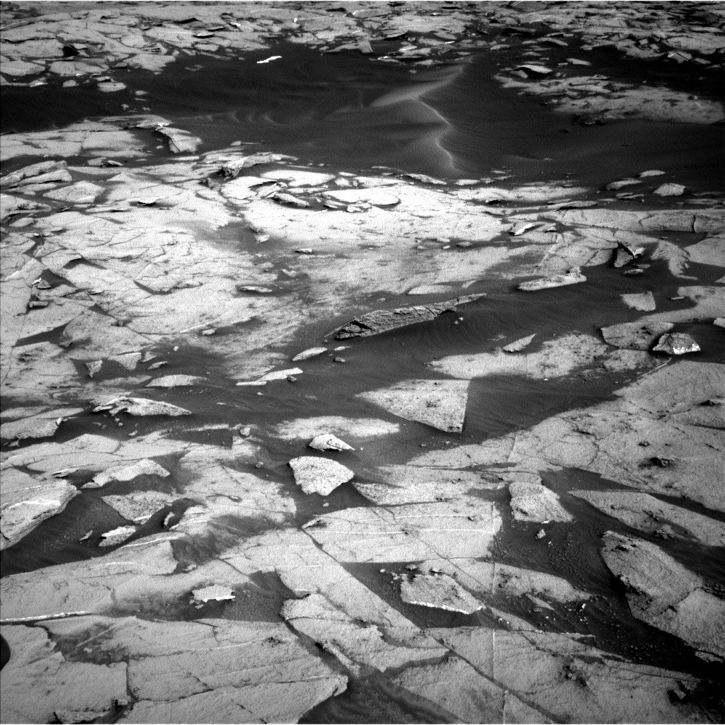 This is a black and white image of large white rocks with marks embedded into the flat, smooth and sandy surface fo Mars.