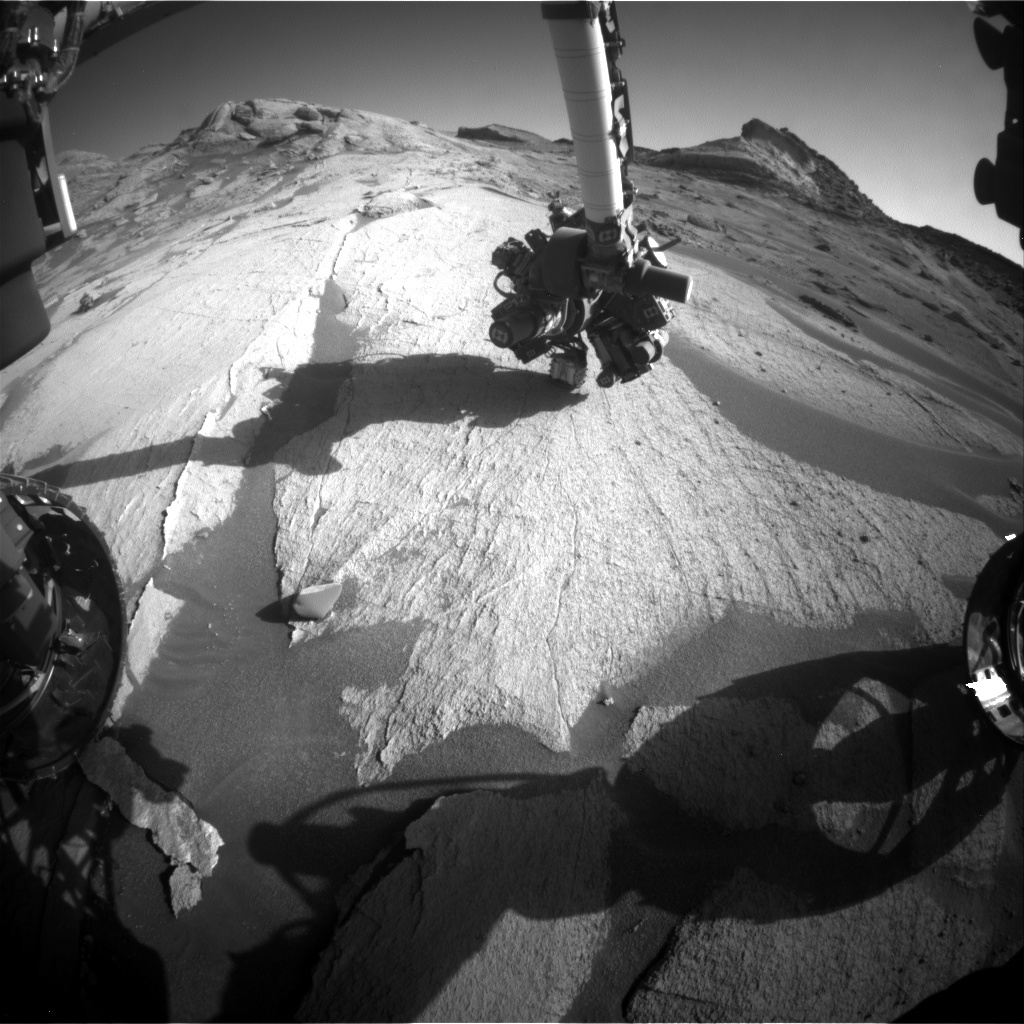 This is a black and white image of the smooth, but slightly rocky surface of Mars. Two hills can be seen in the background. 