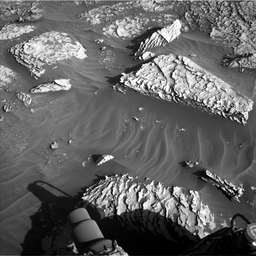 This is a black and white image of large surfaced rocks embedded in smooth sand. There are smaller rocks present as well. The surface of these rocks is rough with lots of cracks. 